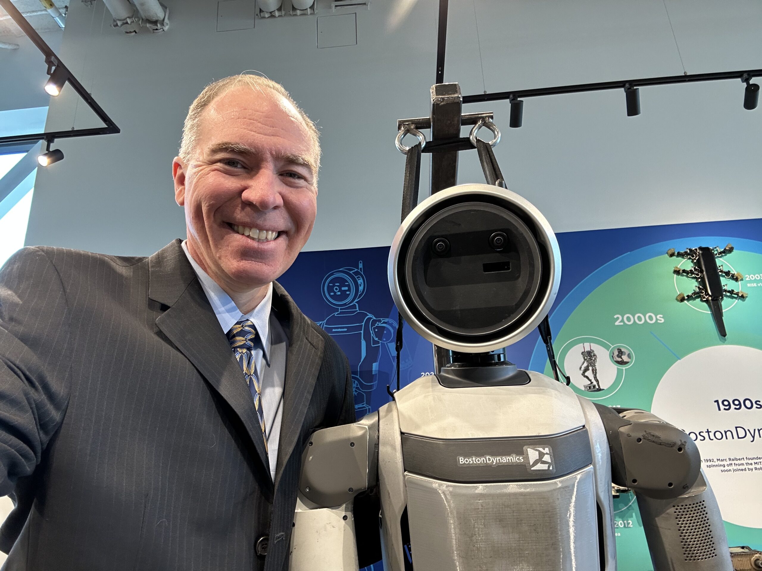 Jason Fiorillo with Boston Dynamics' Atlas humanoid robot, company timeline wall visible in background